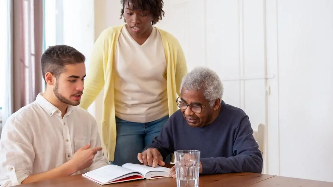 Young adults volunteer at nursing home, helping an elderly man read.