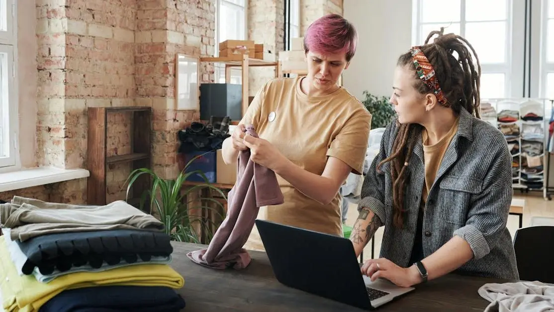 Two women organizing donations and updating a volunteer resume on a laptop in a bright urban space.