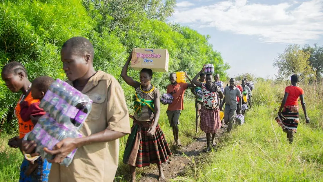 Non profit volunteer group carrying groceries along a sunny rural path to aid local residents
