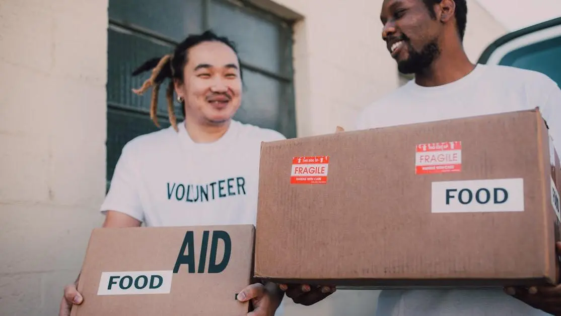 Volunteering travelling: two people carrying food aid boxes, helping local community.
