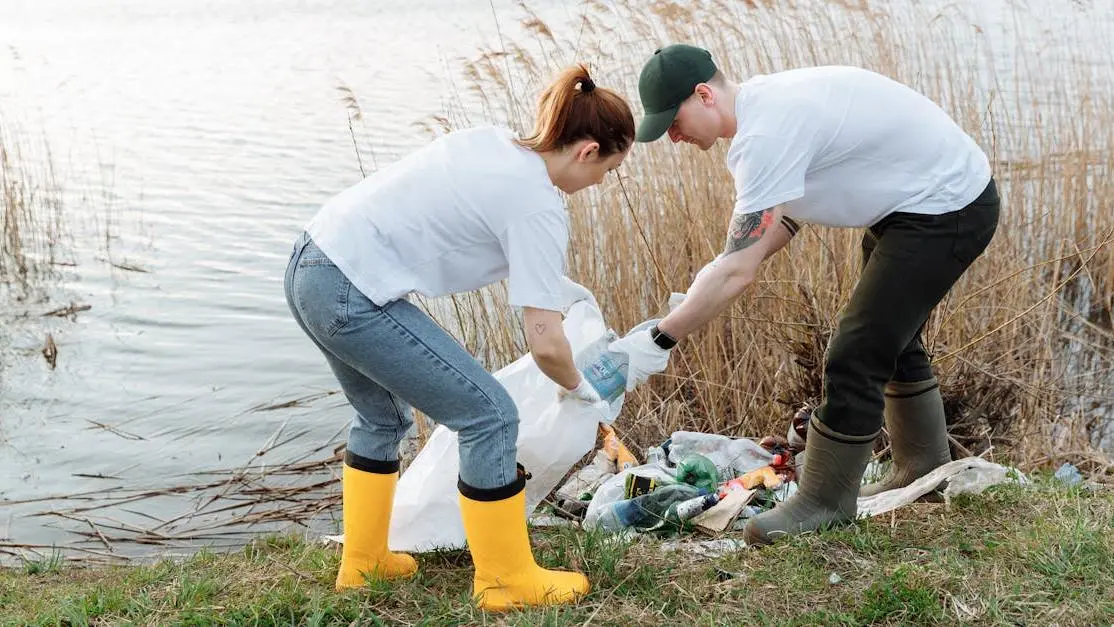 VSO volunteer duo picking up trash by a river, promoting environmental conservation