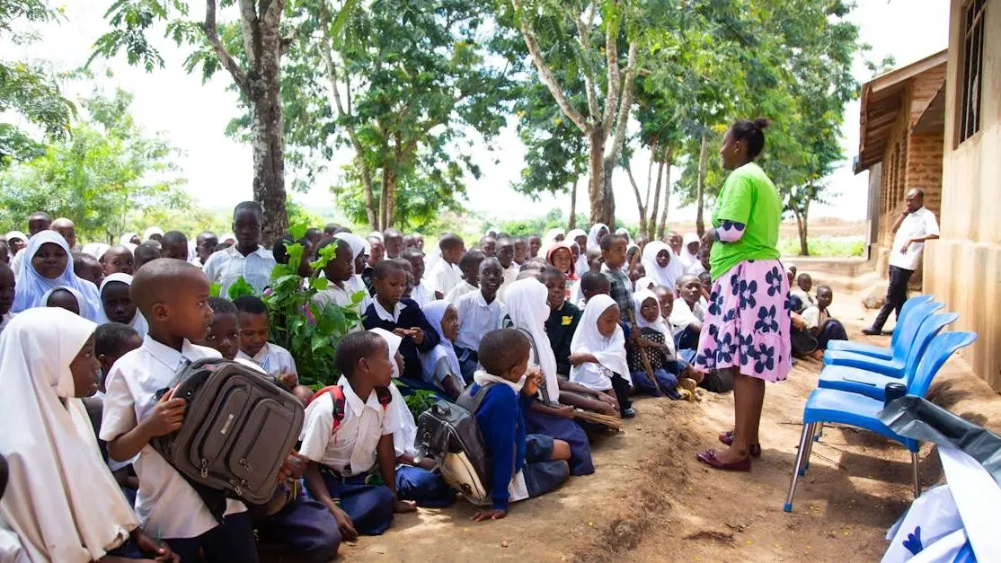 Volunteer in teaching: mentor guiding diverse students in an outdoor class under trees