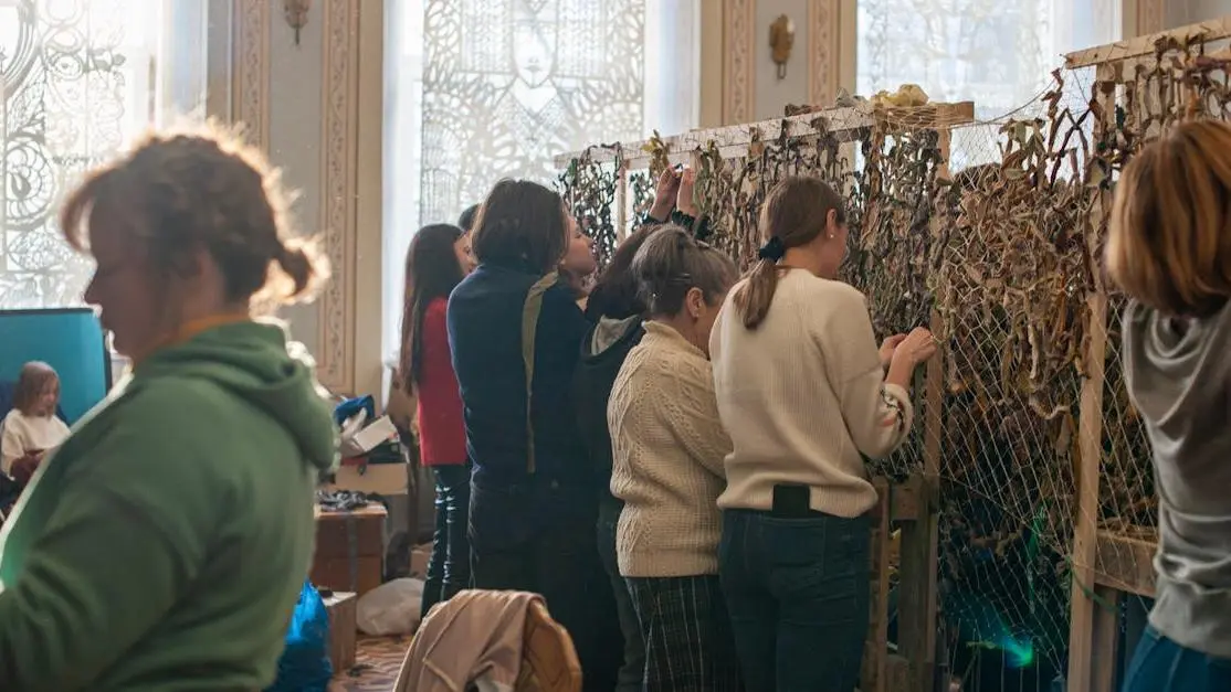 Women weaving camouflage nets indoors, community support and collaboration in human rights volunteering and advocacy