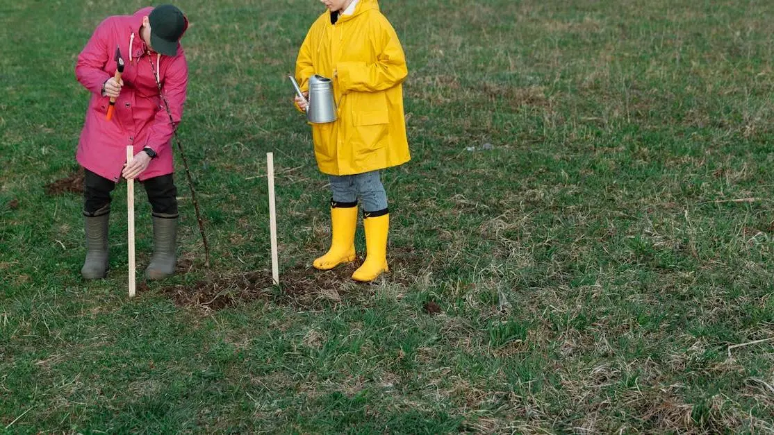 Volunteers tree planting in a grassy field, wearing colorful rain gear and rubber boots