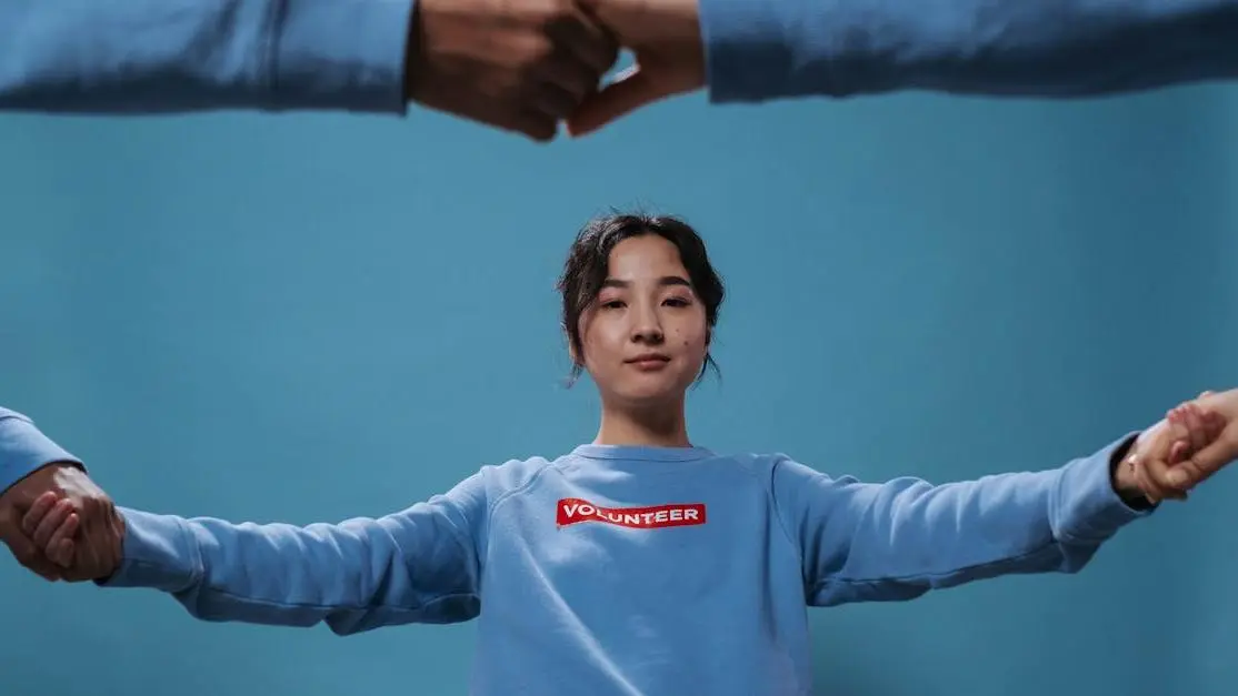 Volunteering for women’s shelters: Asian woman in blue shirt joins hands in a teamwork circle