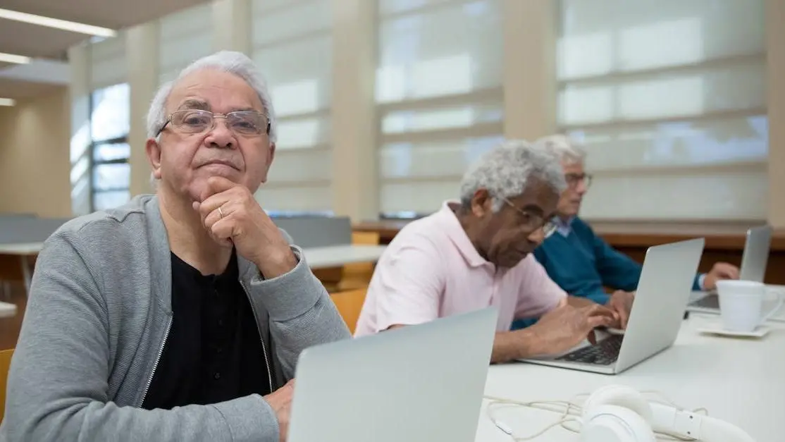 Elderly volunteer opportunities: three senior men using laptops in a library, lifelong learning