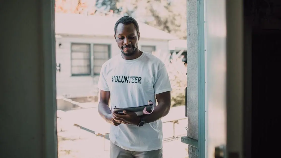 Volunteer opportunities psychology: man in volunteer shirt with tablet at community event doorway